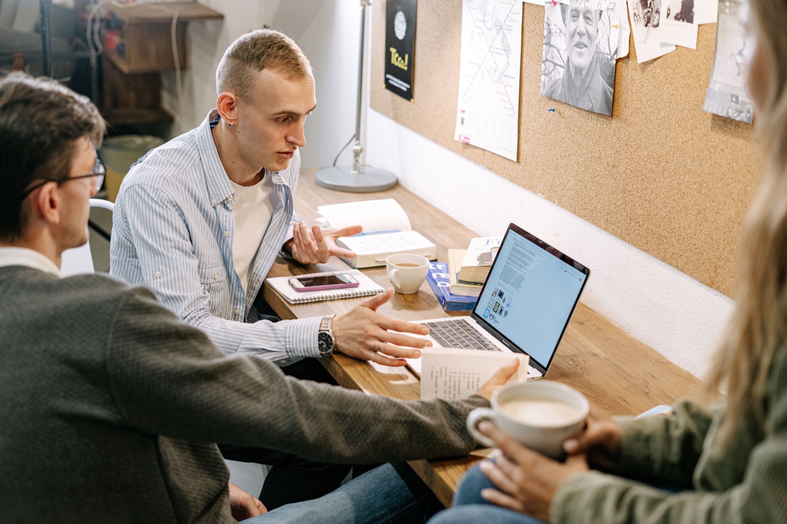 Three people discussing study materials beside an open laptop