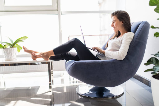 Person working on a laptop while sitting comfortably in a modern chair at home, representing remote work, everyday comfort, and balanced work-from-home routines.