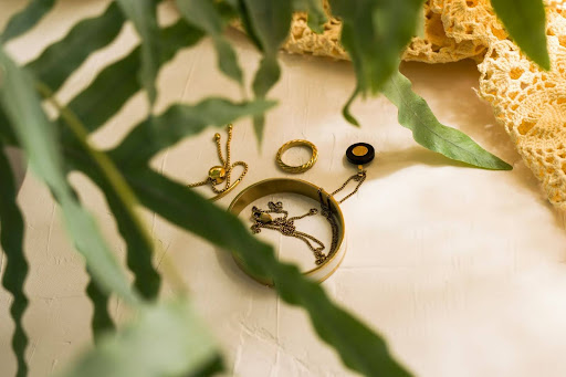Delicate gold jewellery pieces arranged on a neutral surface with green leaves, representing understated elegance, personal style, and timeless accessories.