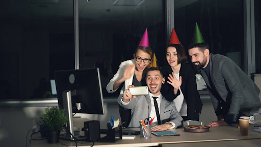 Colleagues celebrating a personal milestone at work Group of coworkers wearing party hats and smiling around a desk, celebrating a workplace milestone in a modern office environment
