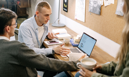 Three people discussing study materials beside an open laptop