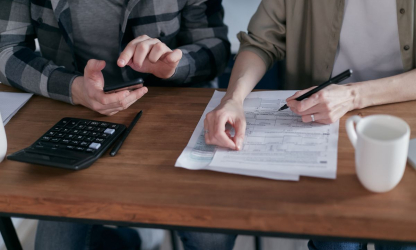 Two people reviewing financial paperwork beside a calculator at a desk.