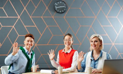 Three professionals sitting at a table, smiling and waving during a meeting, representing teamwork, inclusivity, and positive workplace culture.