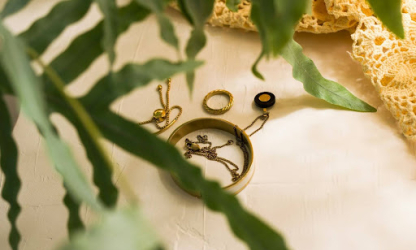 Delicate gold jewellery pieces arranged on a neutral surface with green leaves, representing understated elegance, personal style, and timeless accessories.