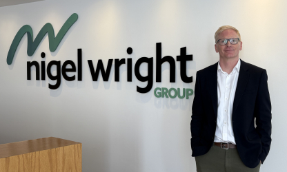 Mark Simpson standing beside the Nigel Wright Group sign in an office reception.