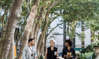 Three colleagues walking together with takeaway drinks in a tree-lined park