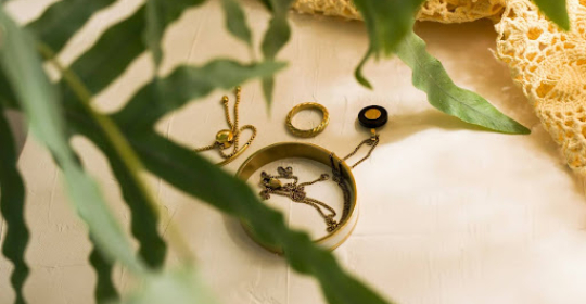 Delicate gold jewellery pieces arranged on a neutral surface with green leaves, representing understated elegance, personal style, and timeless accessories