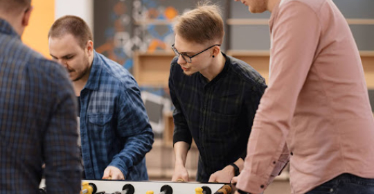 Coworkers playing table foosball together during a team-building activity in a modern office environment